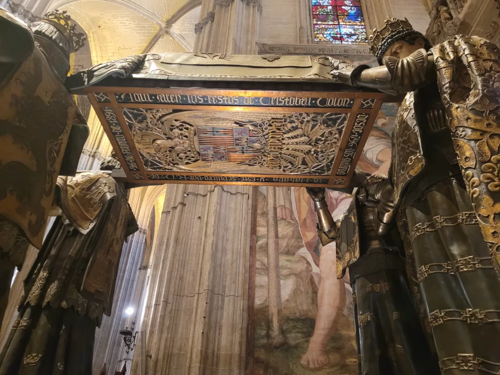 Photo of the underside of Columbus's Tomb inside Seville Cathedral. The Tomb is being held up by four statues, so visitors can see underneath it.