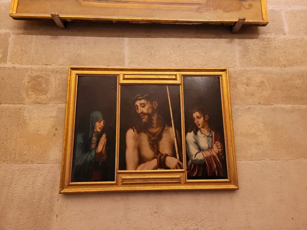 Photo of a piece of art hanging inside Seville Cathedral, depicting Jesus in the center and a woman at each side