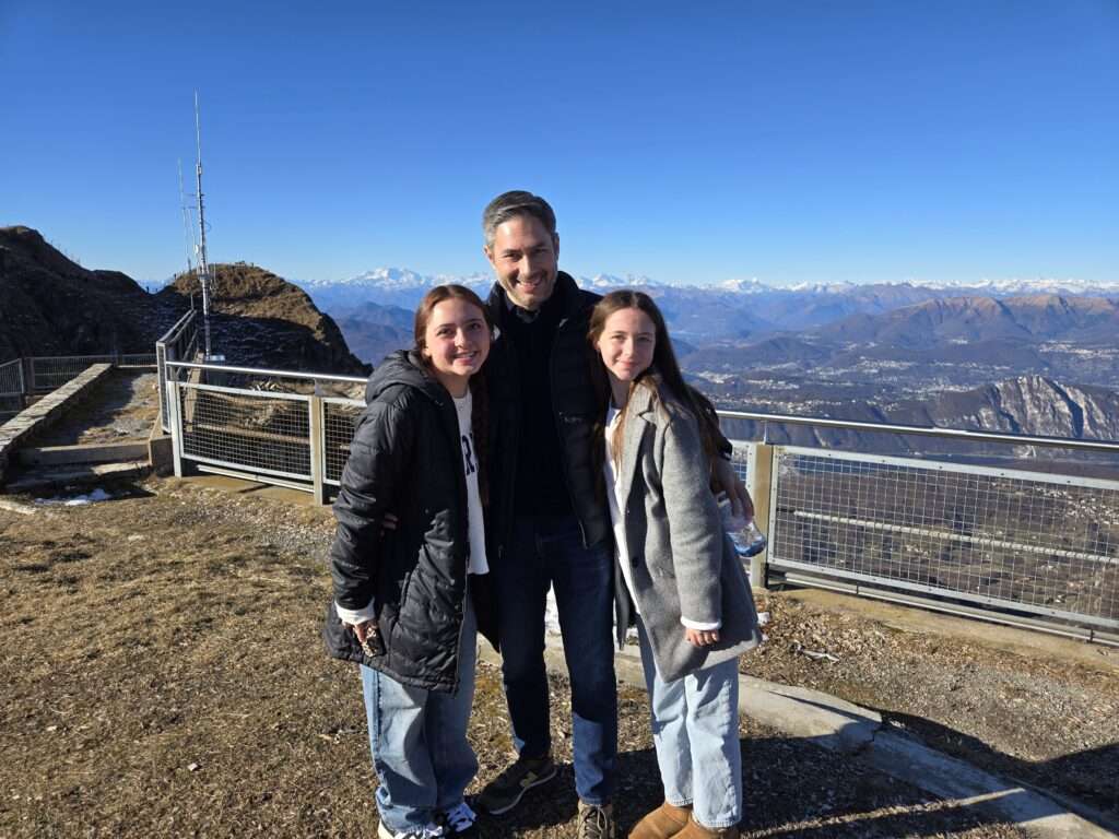 Two teen girls posing with their dad atop Monte Generoso